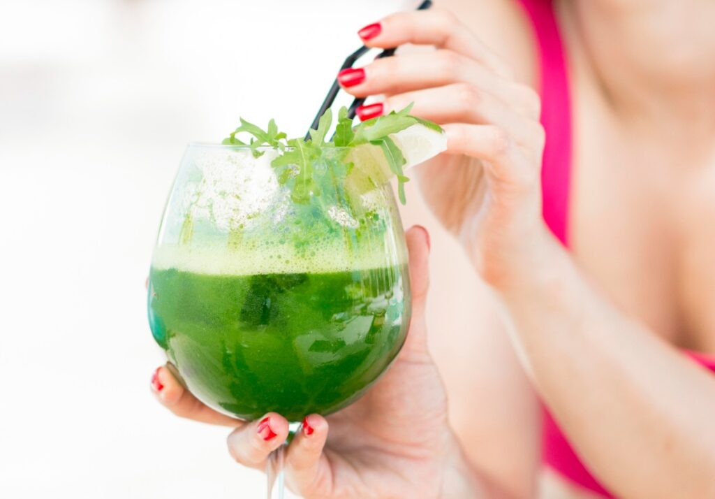 Mulher tomando suco verde numa taça com canudo