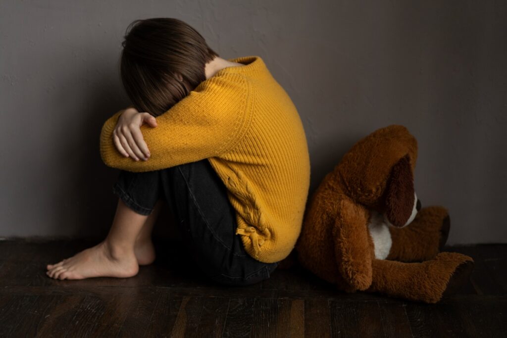 Adolescente com a cabeça entre as pernas ao lado de um urso de pelúcia, representando um adolescente com depressão