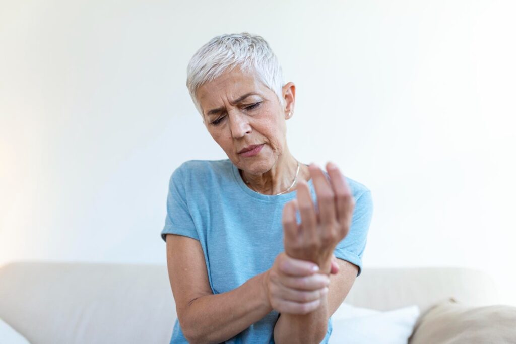 Mulher sentindo dor no pulso, simbolizando os efeitos da osteoporose.