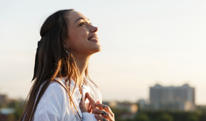 Mulher sorrindo e olhando para o céu, representando a importância do autocuidado e da conexão com o ambiente.