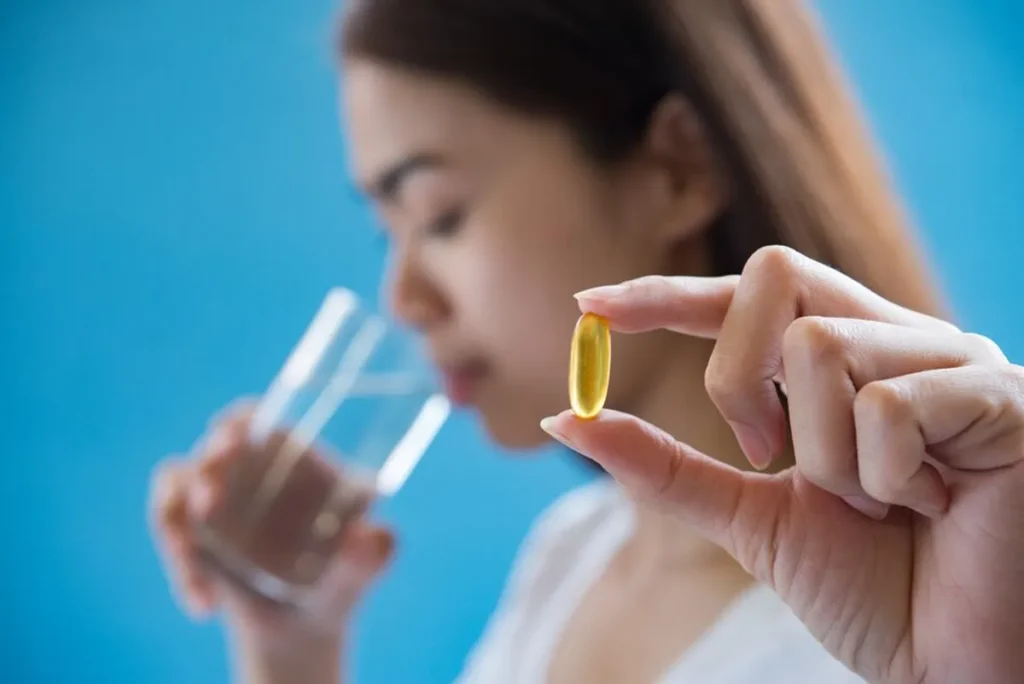 Mulher segurando cápsula de vitamina D antes de tomar com um copo de água