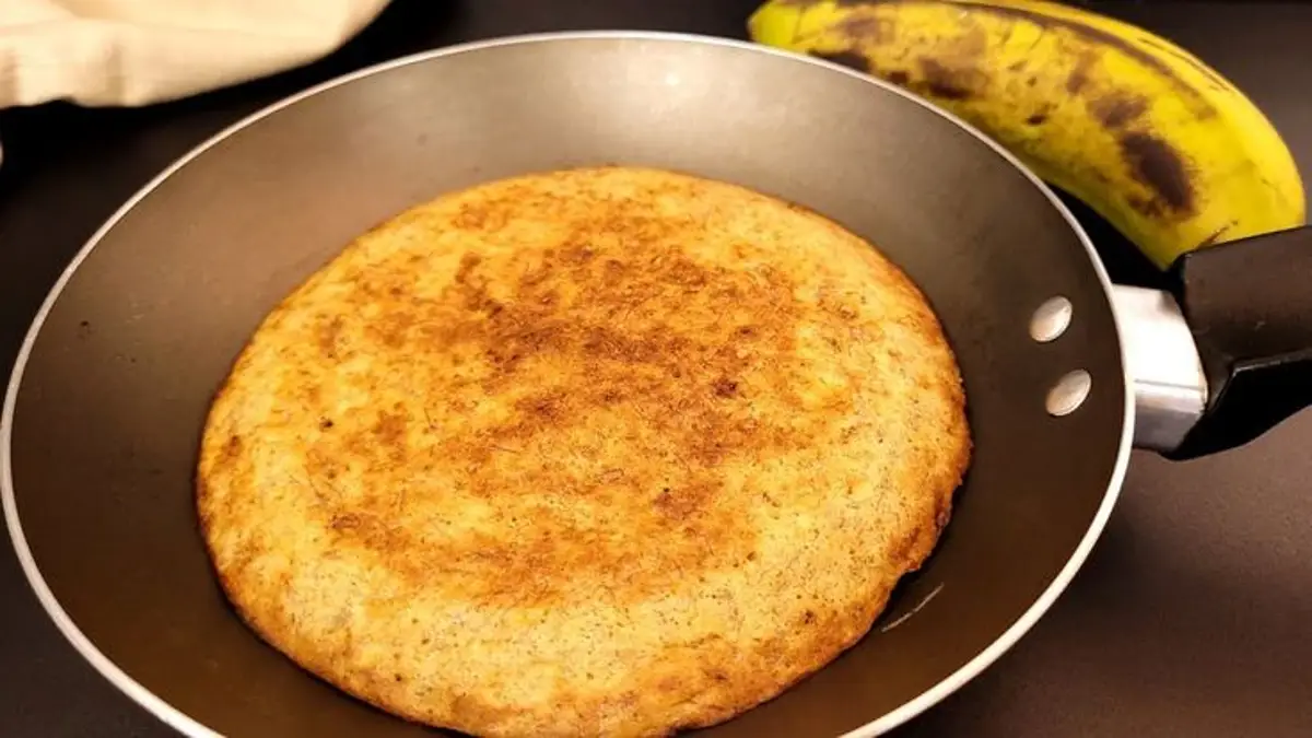 Pão de aveia de frigideira com aparência dourada, pronto para consumo, com um banana ao fundo.