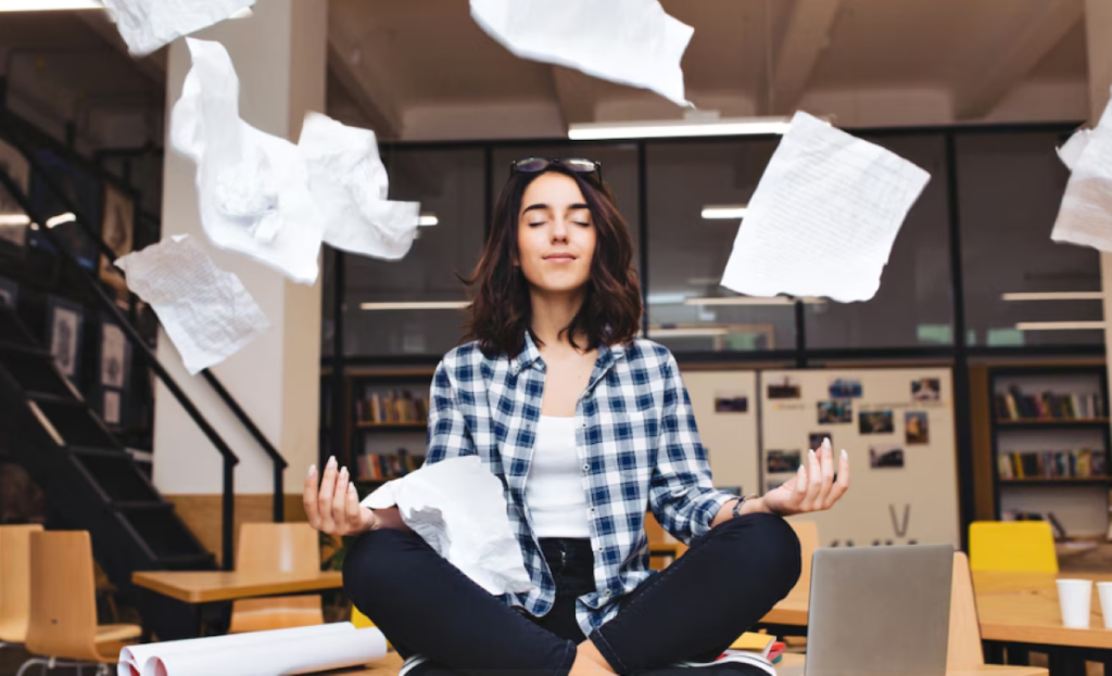 Mulher meditando enquanto papéis flutuam ao seu redor em um ambiente de trabalho, representando saúde mental no trabalho.