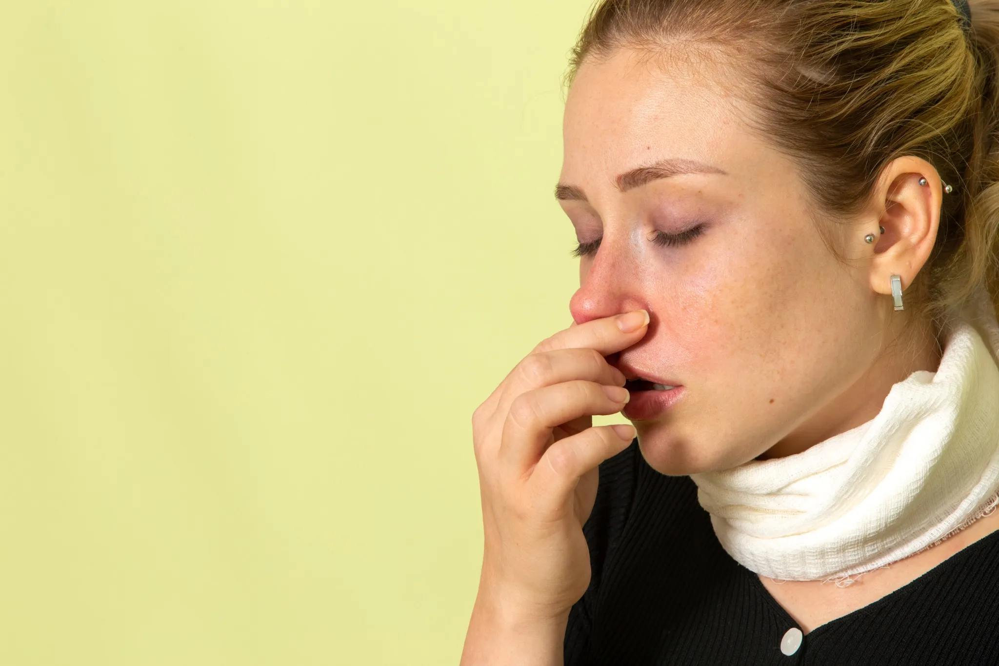 Mulher com lenço no pescoço, sentindo-se mal devido a uma alergia a medicamento, limpando o nariz.