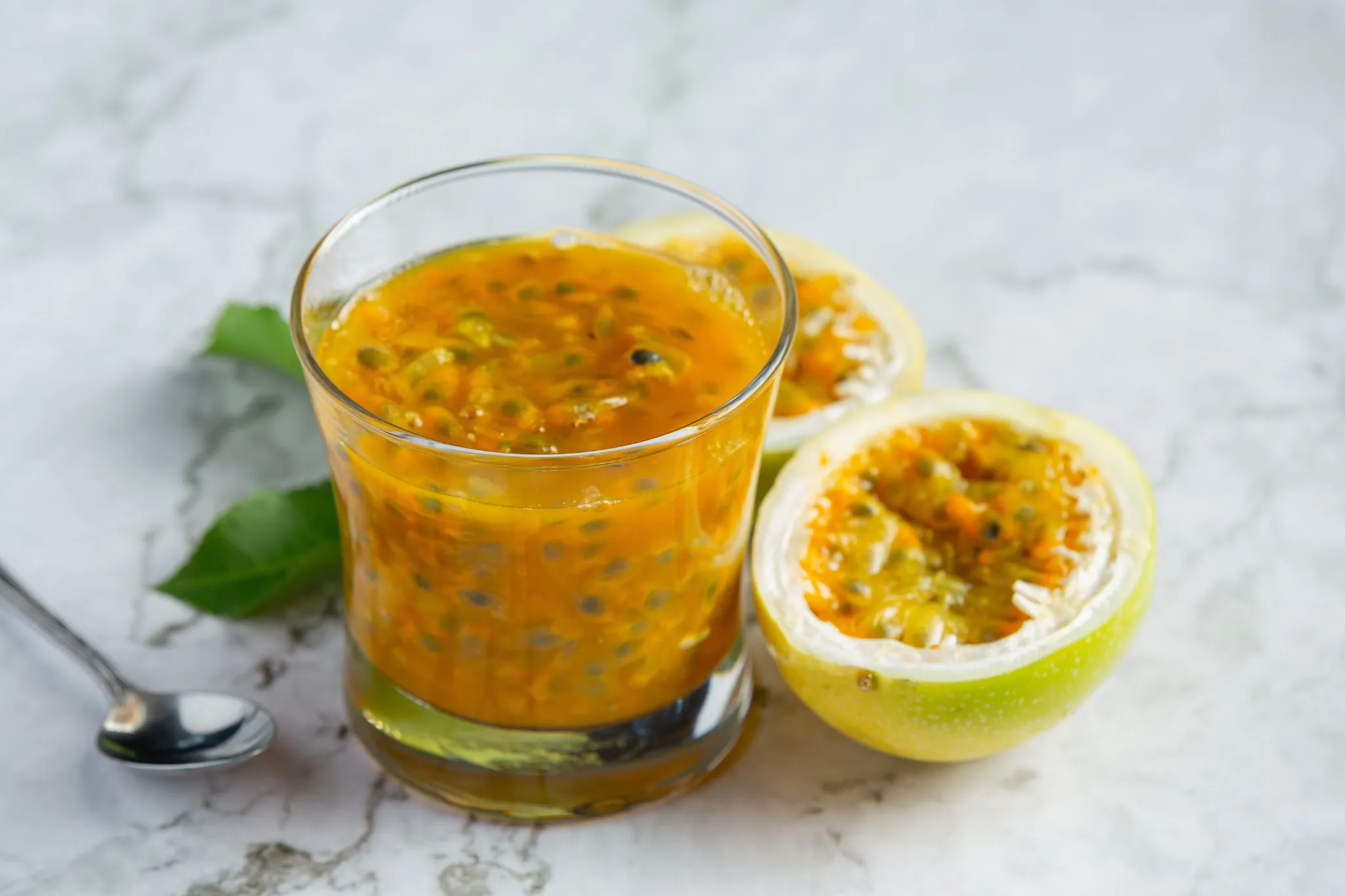 Suco de maracujá natural com polpa visível em um copo, ao lado de uma fruta cortada ao meio.