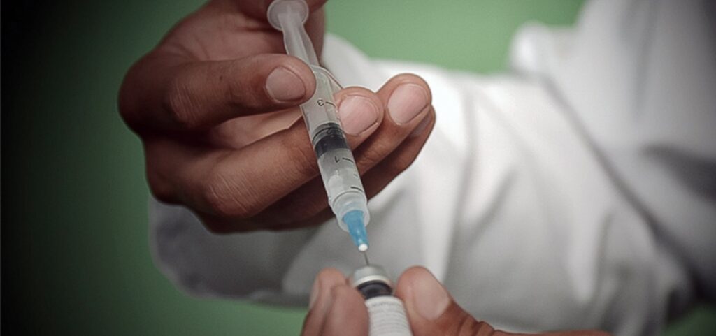 Imagem de uma seringa sendo preparada com vacina, ilustrando a recomendação da OMS de injeção semestral para prevenção do HIV.