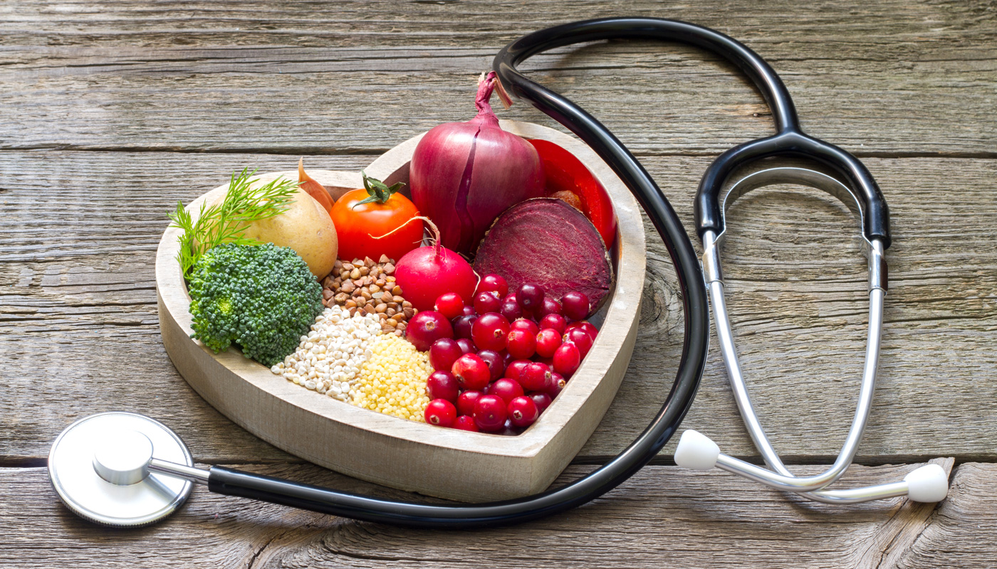 Alimentos saudáveis em um pote de coração com um estetoscópio, representando a importância da alimentação na saúde do coração.